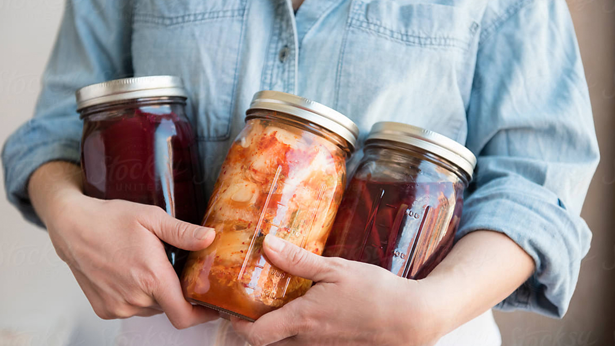 Womans arms holding three larger jar full of fermenting foods.
